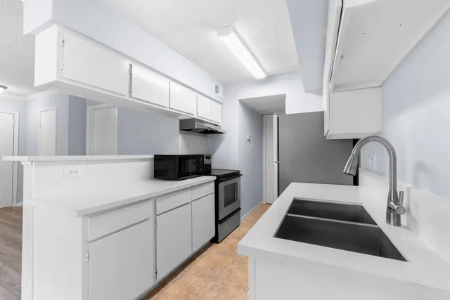 a kitchen with stainless steel appliances a sink dishwasher a stove a refrigerator and white cabinets with wooden floor