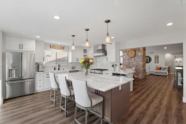 a large white kitchen with granite countertop a stove a sink a dining table and chairs