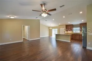 a view of an empty room and kitchen with wooden floor