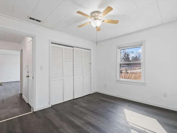 an empty room with wooden floor chandelier fan and windows