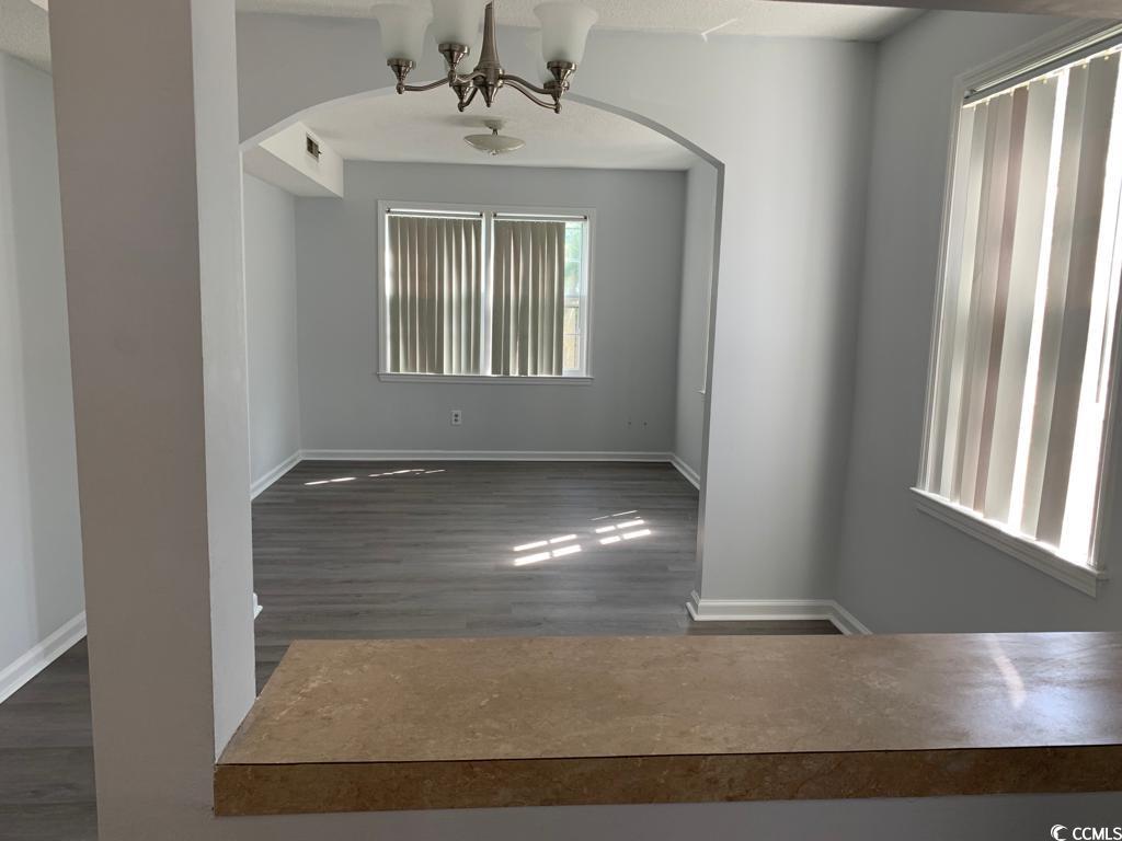105 South Merriman Road, Unit 1 Georgetown, SC 29440 - Photo 15 of 22 Empty room featuring dark wood finished floors, arched walkways, and a chandelier