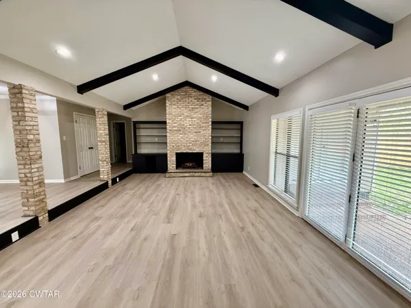 an empty room with wooden floor fireplace and windows