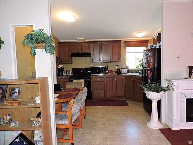 915 North 5000 W Road Hinckley, UT 84635 - Photo 7 of 27 Kitchen area featuring wood-finish cabinetry, black appliances, light-toned flooring, a window with a valance,