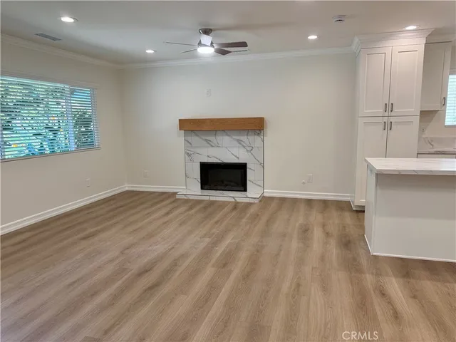 an empty room with wooden floor a ceiling fan a fireplace and windows