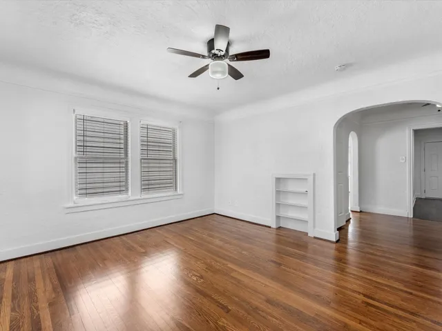 an empty room with wooden floor chandelier fan and windows