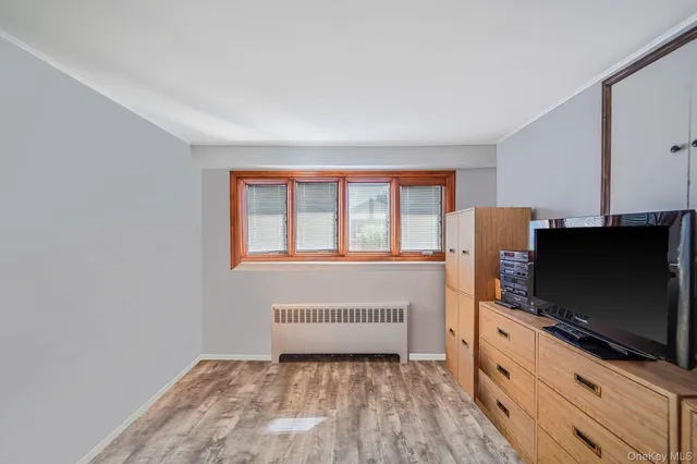 a living room with a flat screen tv on dresser and a window