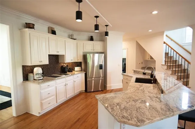 a kitchen with stainless steel appliances granite countertop a refrigerator a stove a sink dishwasher and white cabinets with wooden floor