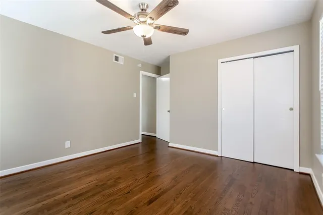 an empty room with wooden floor ceiling fan and windows