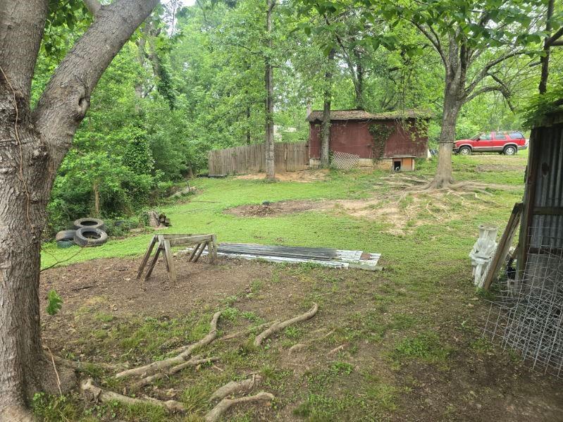 390 Campground Road Trinity, TX 75862 - Photo 35 of 37 Expansive yard featuring mature trees, a red outbuilding with natural vine growth, and a partial privacy fence