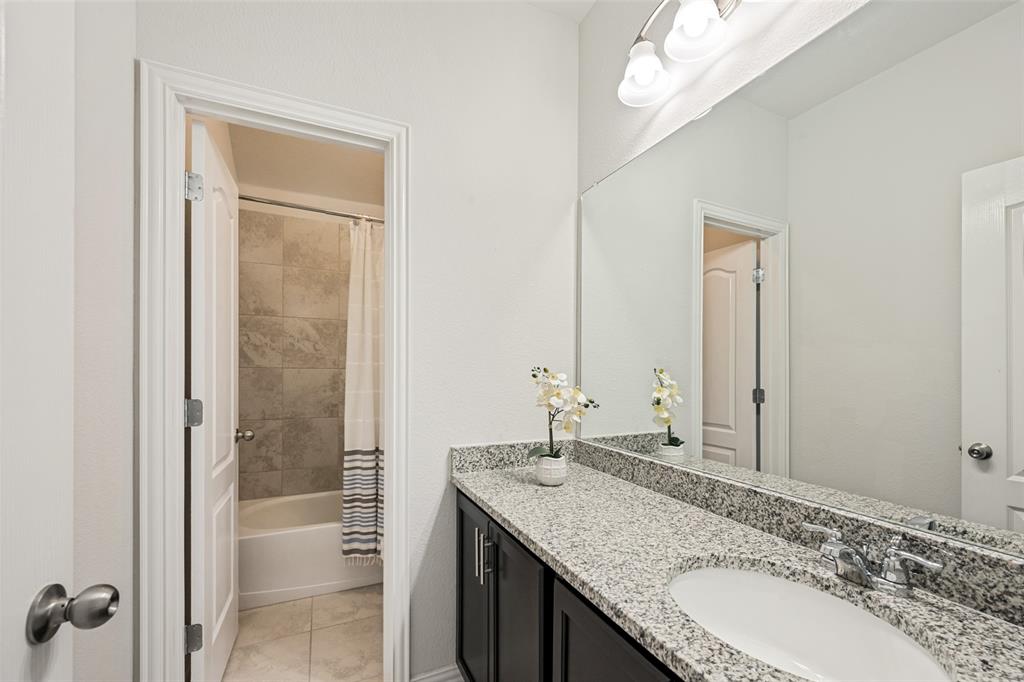 15725 Preble Road Fort Worth, TX 76177 - Photo 15 of 25 Spa-inspired master bathroom featuring a dual-sink vanity with speckled stone countertop, sleek matte black hardware, and an expansive framed mirror illuminated by overhead lighting