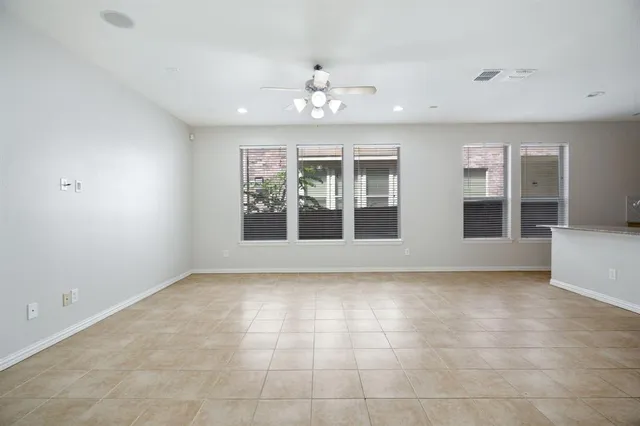 a view of an empty room with chandelier fan and kitchen view