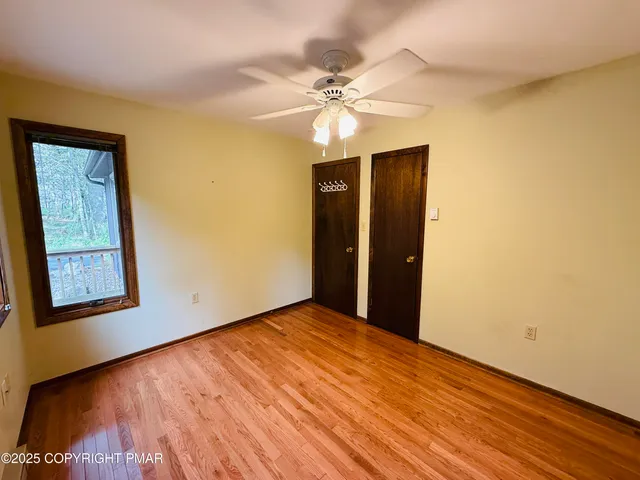 a view of an empty room with wooden floor and a ceiling fan
