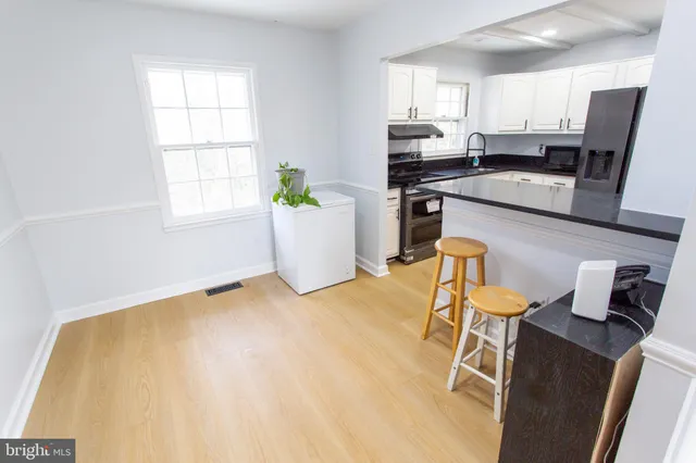 a kitchen with stainless steel appliances kitchen island granite countertop a refrigerator a stove a sink and white cabinets with wooden floor