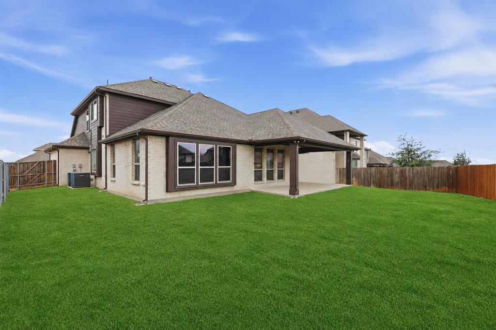 924 Timber Ridge Drive Justin, TX 76247 - Photo 32 of 32 Expansive green yard featuring a covered patio, tan brick exterior, dark wood-finish siding, multiple windows, and partial perimeter fencing