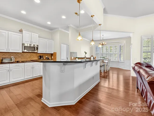 a large kitchen with stainless steel appliances granite countertop a stove a sink a refrigerator and white cabinets with wooden floor