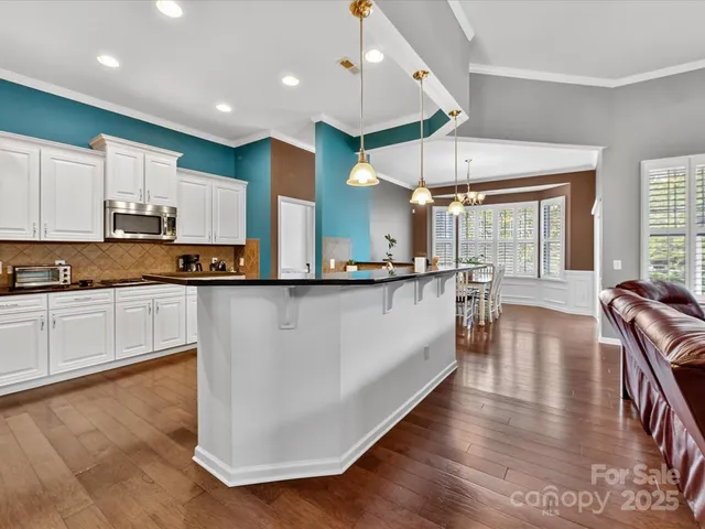 a large kitchen with stainless steel appliances granite countertop a stove a sink a refrigerator and white cabinets with wooden floor