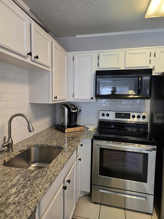 18333 Roehampton Drive, Unit 1516 Dallas, TX 75252 - Photo 1 of 1 Kitchen with a sink, electric range, white cabinetry, light stone counters, and black microwave