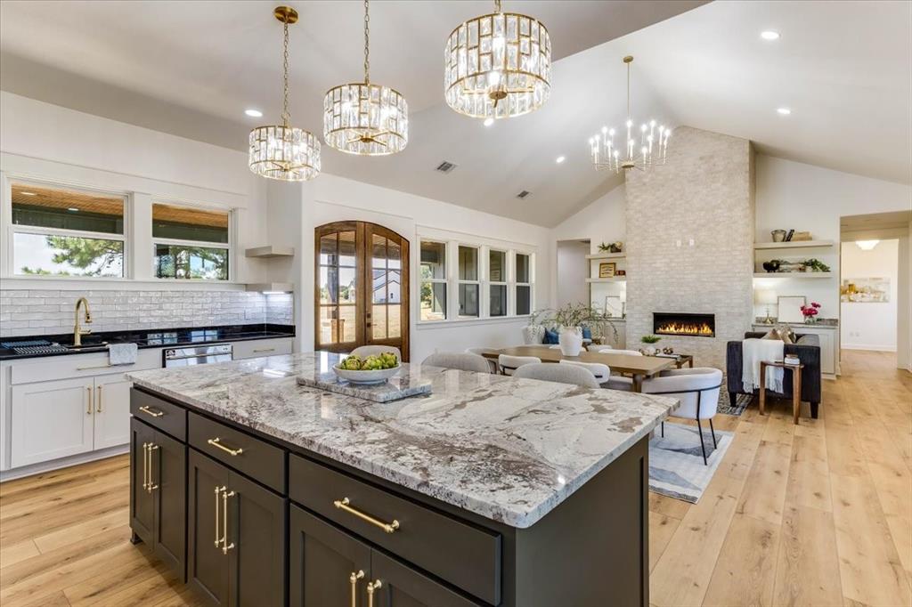 242 Private Road Mount Pleasant, TX 75455 - Photo 14 of 40 Open-concept living space with vaulted ceilings, a stone fireplace, wood-finish flooring, and a kitchen island with a granite countertop and pendant lighting