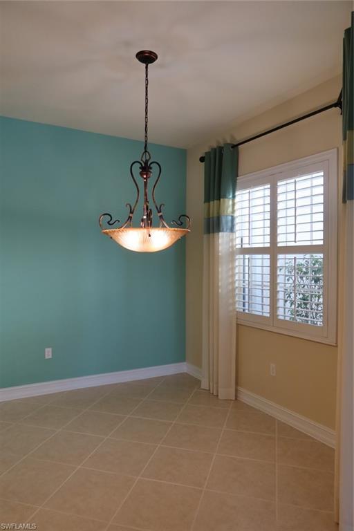 7168 Lemuria Circle, Unit 1701 Naples, FL 34109 - Photo 12 of 39 Room featuring neutral tile flooring, white baseboards, and a prominent chandelier with an antique bronze finish and frosted glass bowl