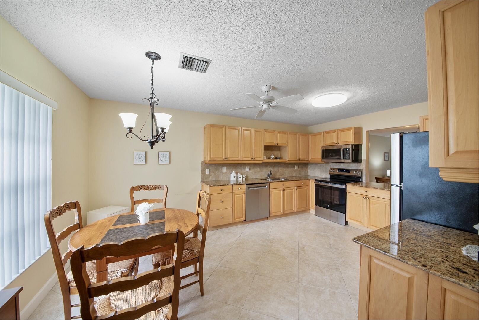 5222 Privet Place, Unit B Delray Beach, FL 33484 - Photo 13 of 27 a kitchen with stainless steel appliances kitchen island granite countertop a refrigerator a stove a sink dishwasher a dining table and chairs with wooden floor