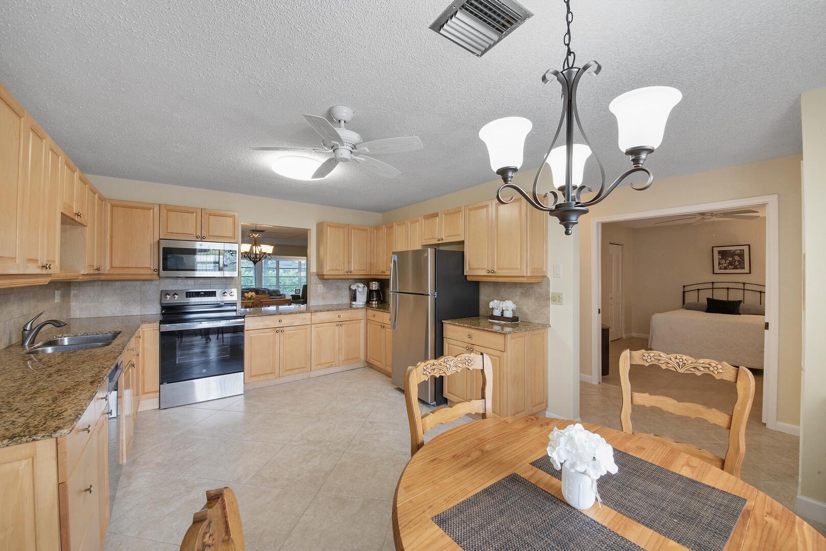 5222 Privet Place, Unit B Delray Beach, FL 33484 - Photo 14 of 27 a kitchen with stainless steel appliances kitchen island granite countertop a refrigerator a stove top oven a dining table and chairs with wooden floor