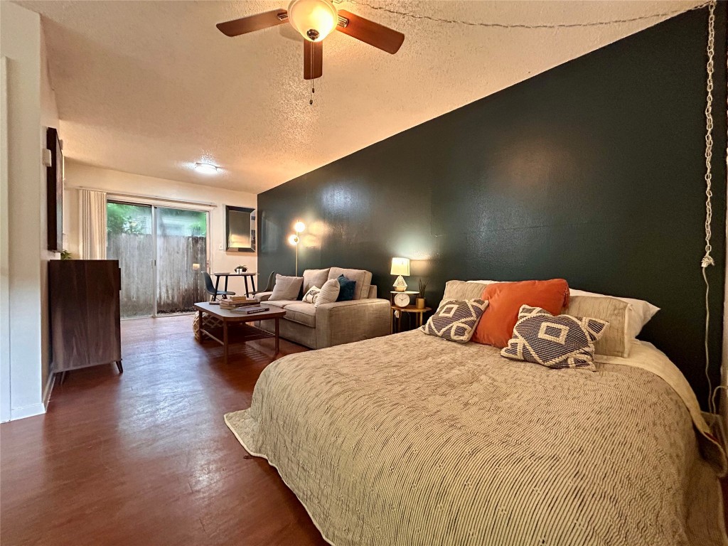 Bedroom with a textured ceiling, dark wood-style flooring, access to exterior, ceiling fan, and lofted ceiling