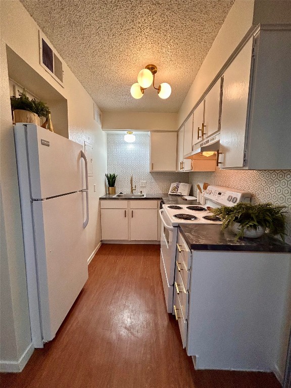 4209 Avenue B, Unit 206 Austin, TX 78751 - Photo 5 of 8 Kitchen with dark countertops, white appliances, dark wood-style flooring, under cabinet range hood, and a textured ceiling