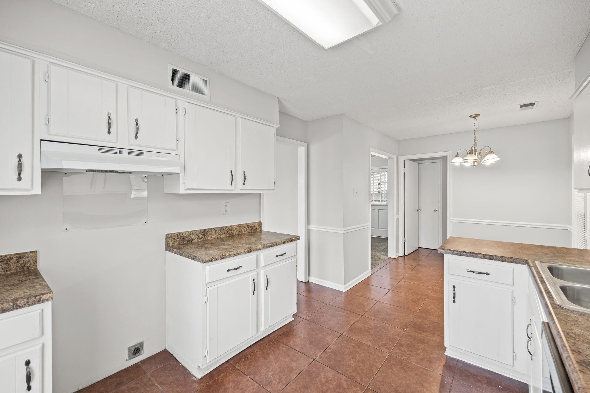 Kitchen with white cabinets, decorative light fixtures, under cabinet range hood, a chandelier, and a textured ceiling