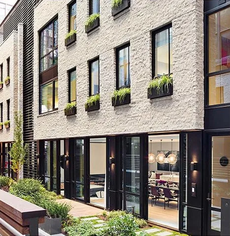 a view of a brick house with plants and large tree