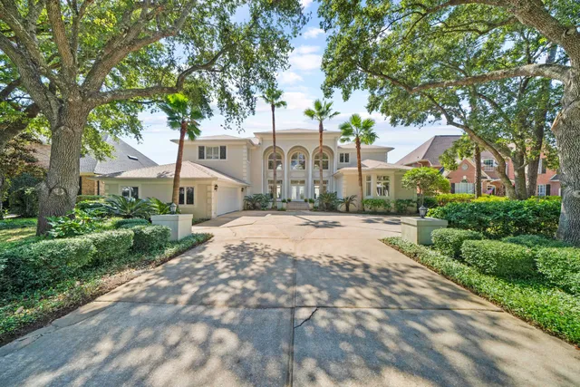 a view of a white house with a big yard plants and large trees