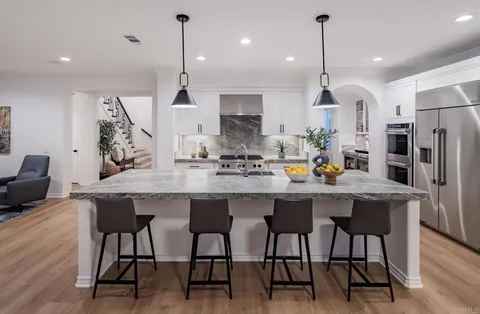 a kitchen with stainless steel appliances kitchen island granite countertop a dining table chairs and white cabinets