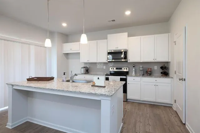a kitchen with stainless steel appliances granite countertop a sink a stove a refrigerator and white cabinets