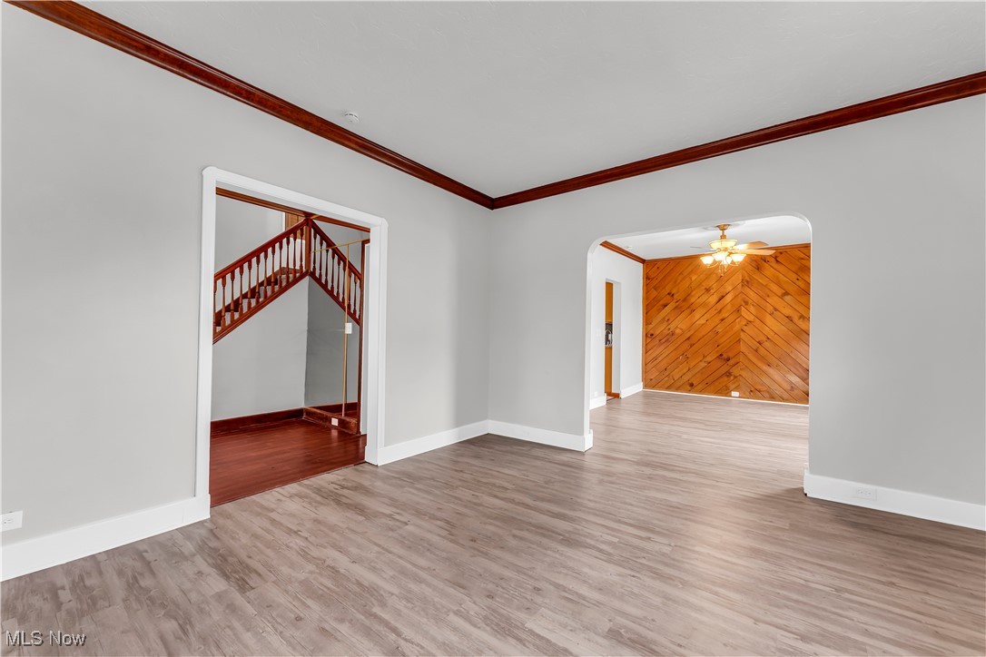 3374 Fulton Road Cleveland, OH 44109 - Photo 6 of 27 Unfurnished room with ornamental molding, wooden walls, light wood-type flooring, ceiling fan, and arched walkways