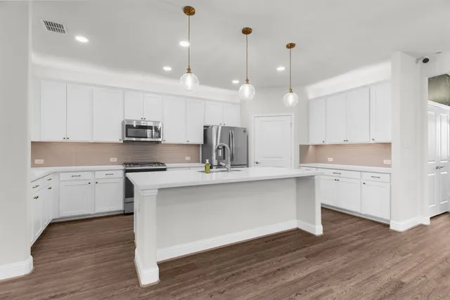 a kitchen with stainless steel appliances granite countertop a sink a stove a refrigerator and island with wooden floor