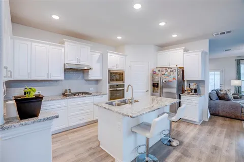 a kitchen with stainless steel appliances kitchen island granite countertop a refrigerator oven a stove a sink a dining table and chairs with wooden floor
