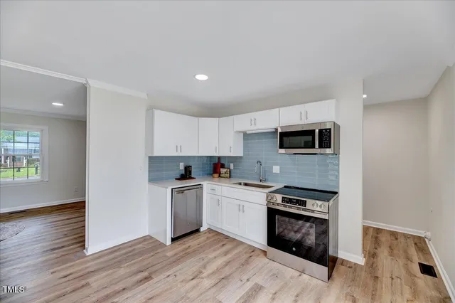 a kitchen with stainless steel appliances granite countertop a stove top oven a sink dishwasher and white cabinets with wooden floor