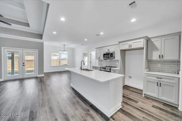 a large white kitchen with wooden floor and stainless steel appliances