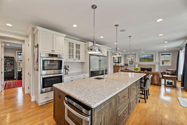 a kitchen with stainless steel appliances granite countertop a kitchen island a stove a refrigerator a oven a sink a dining table and chairs with wooden floor