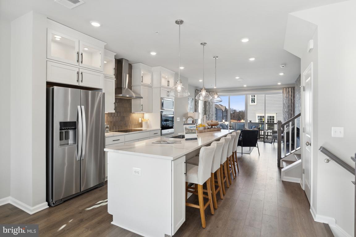 a kitchen with stainless steel appliances kitchen island granite countertop a dining table chairs refrigerator and white cabinets