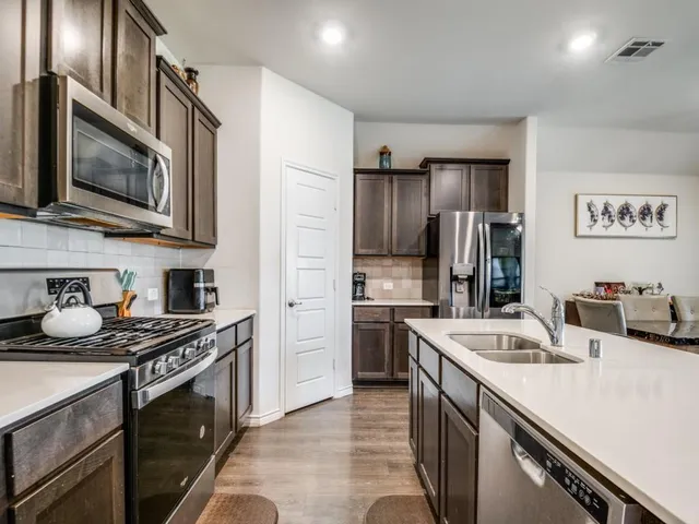 a kitchen with stainless steel appliances granite countertop a refrigerator a stove top oven a sink dishwasher and wooden cabinets with wooden floor