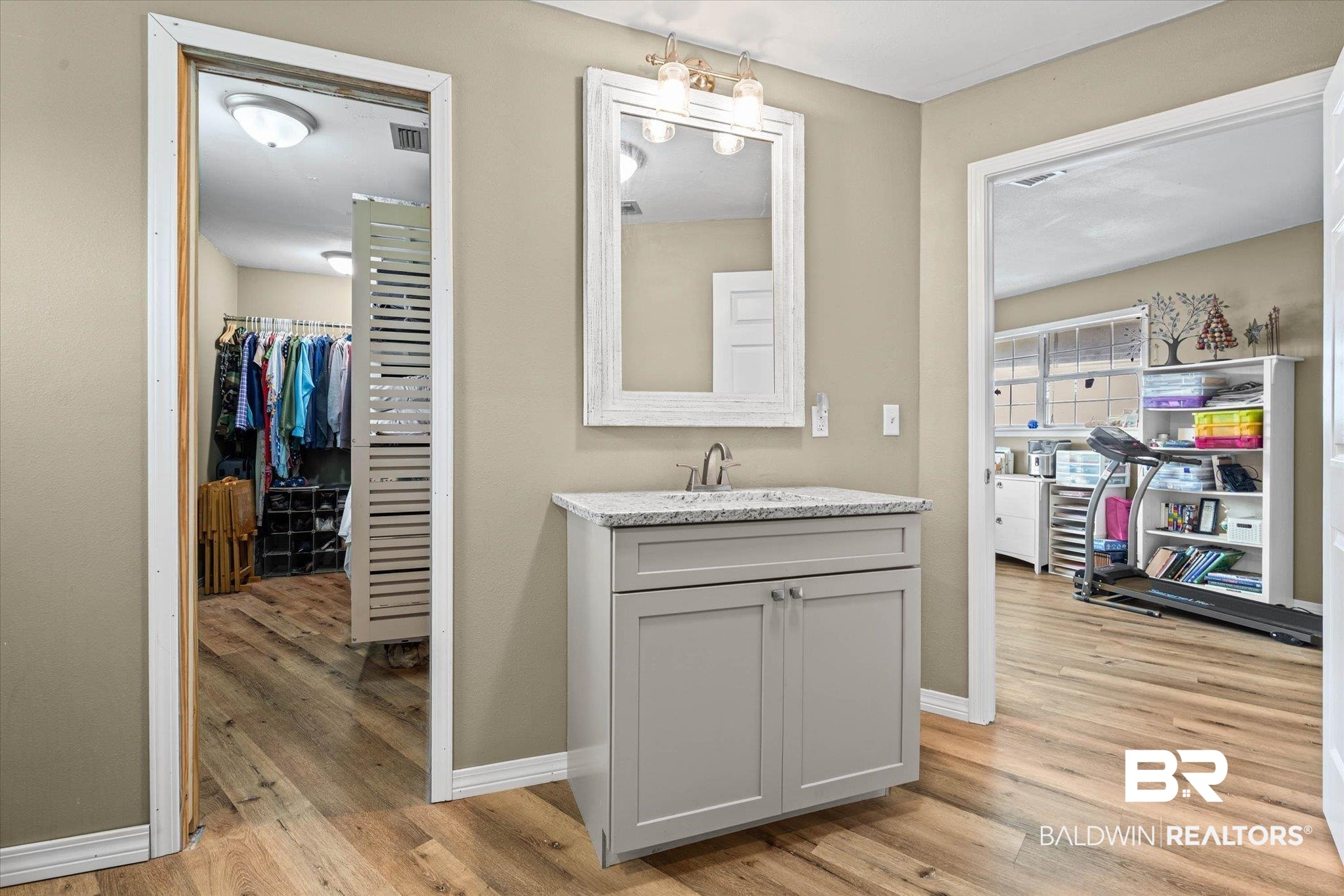 9100 Shell Belt Road Coden, AL 36523 - Photo 14 of 38 Vanity area featuring wood-finish flooring, a light gray vanity cabinet, a granite-finish countertop with an undermount sink, and a framed mirror with overhead lighting