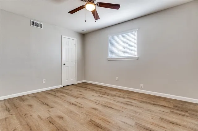 an empty room with wooden floor ceiling fan and windows