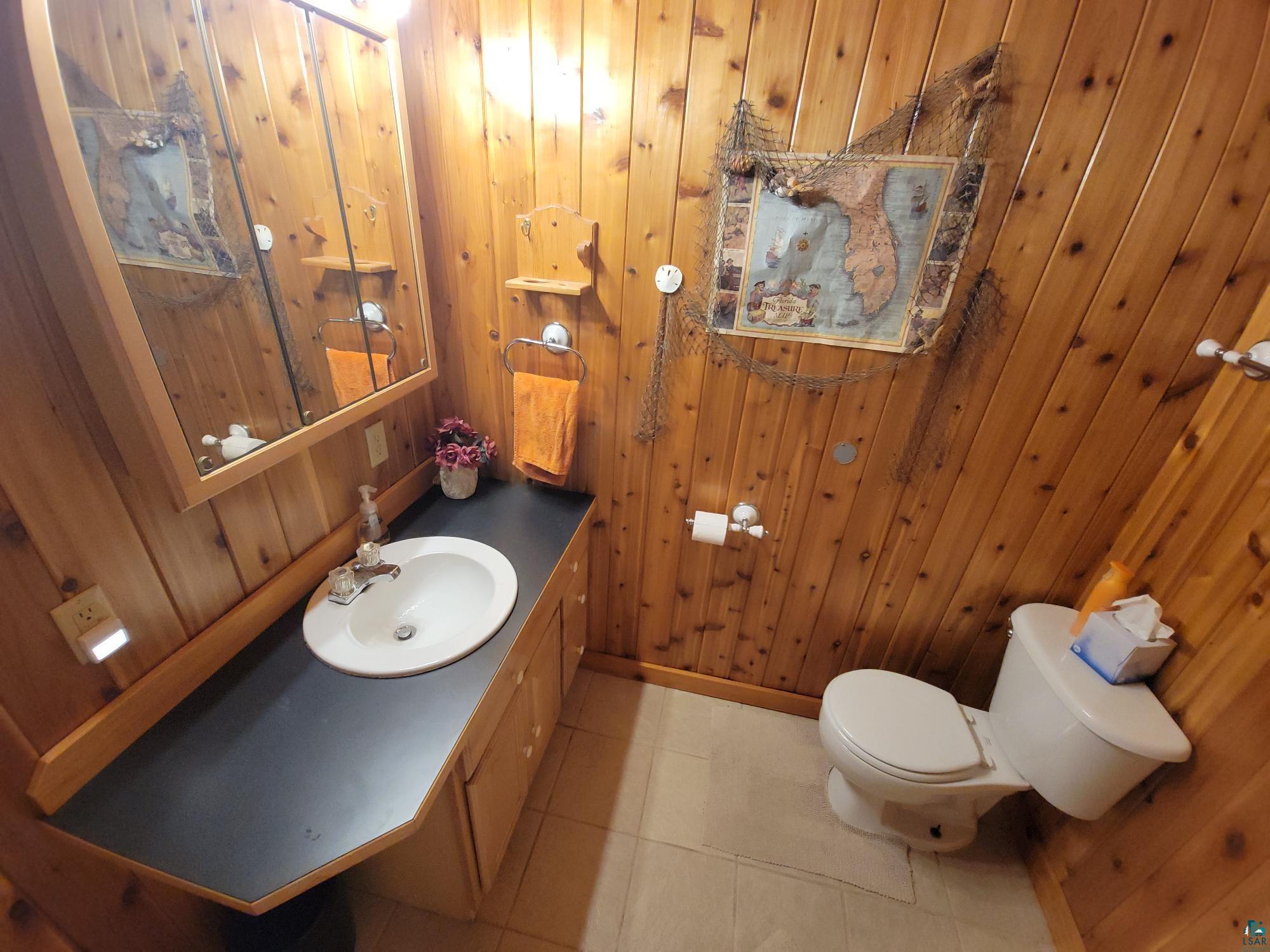 181 Linnell Road Grand Marais, MN 55604 - Photo 63 of 77 Wood paneling throughout, built-in wooden vanity with black countertop, integrated sink, and wall-mounted mirror