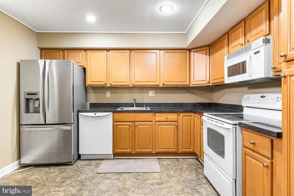 a kitchen with stainless steel appliances granite countertop a refrigerator a sink and white cabinets next to a window