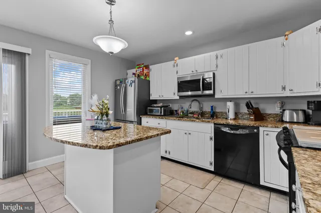 a kitchen with stainless steel appliances granite countertop a sink dishwasher a stove a refrigerator and a dining table with wooden cabinet