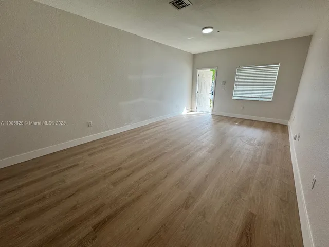 a view of an empty room with wooden floor and a window