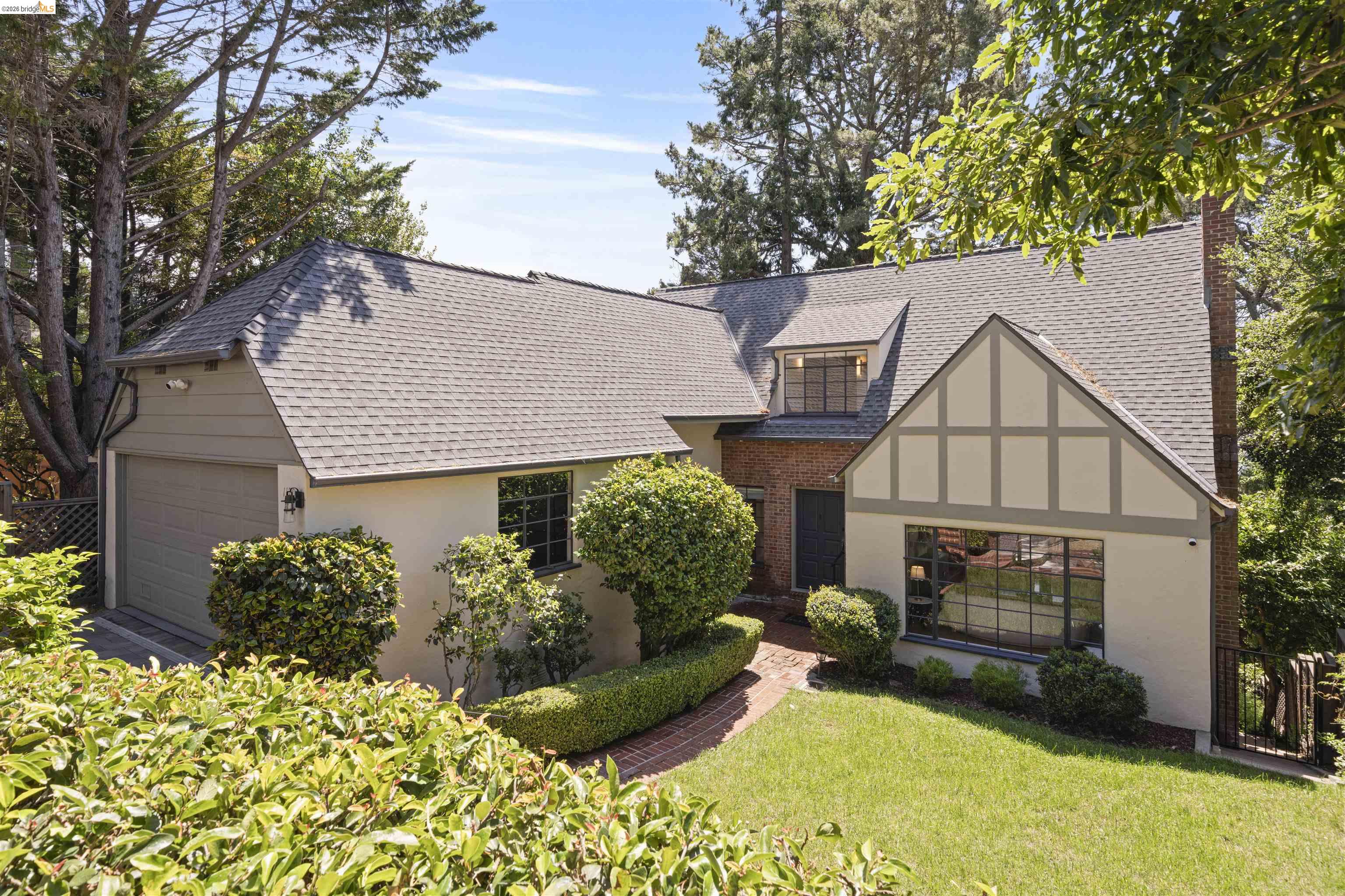 Tudor-style house featuring stucco siding, a chimney, brick siding, a shingled roof, and a garage