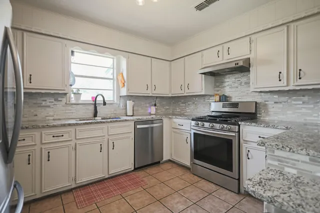 a kitchen with granite countertop white cabinets sink and stainless steel appliances
