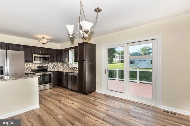 a kitchen with stainless steel appliances granite countertop a refrigerator a sink dishwasher a stove and a dining table with wooden floor