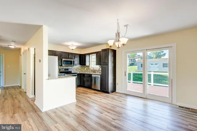 a open kitchen with stainless steel appliances granite countertop a refrigerator oven a sink dishwasher and white cabinets with wooden floor